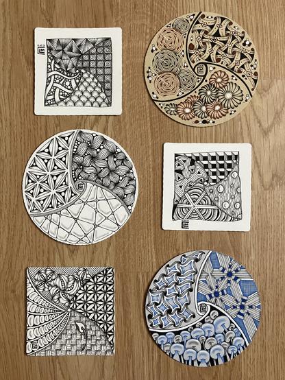 Three square tiles, each containing four patterns, and three round Zendala tiles, each containing three patterns, laid out on a wooden floor. 