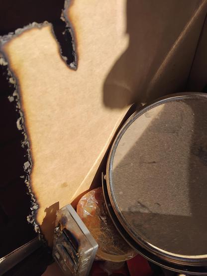 Photo of a cardboard box with one horozontal charred edge and a vertical charred edge and a charred track going 60mm down into the back piece of cardboard from the top charred edge. There is a magnifying shaving mirror in the right of the photo and a melted plastic razor blade holder in the bottom left.

I have in another life taken 200 small bales of hay out of a shed and stood them in pairs in the paddock when they began to steam in the shed. Baled too green. They can combust.