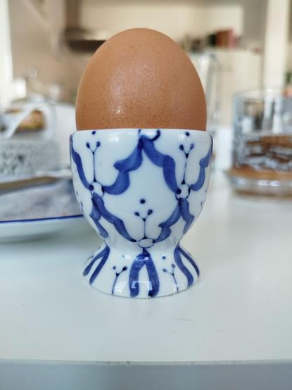Ein braunes ei in einem blau weißen Porzellan Eierbecher. Das Dekor sieht aus Versehen auf der einen Seite so aus wie ein Gesicht