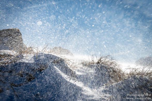 In this image, we see snow falling gently on a hill, creating a serene winter scene.  The landscape is covered in a blanket of snow, with a clear sky overhead. The overall mood is peaceful and cold, evoking feelings of tranquility and isolation. The image captures the essence of winter, with freezing temperatures and a mountain in the background. The scene is perfect for those who enjoy nature and the beauty of snowy landscapes.