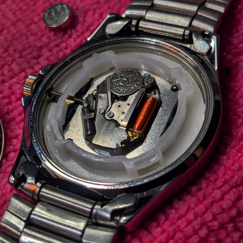 Zoomed in image of the opened back of a stainless steel Casio Quartz watch showing the movement with the battery removed. Pink cloth as background.
