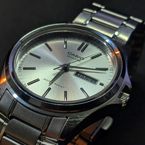 Oblique viwe of a stainless steel Casio Quartz analog watch with a calendar complication. Has a brushed metal dial and hands.