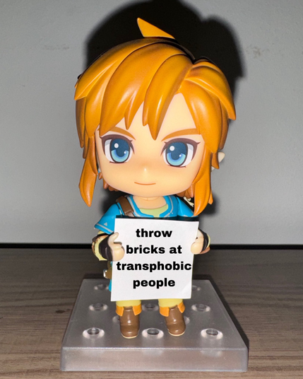 A figurine of Link from The Legend of Zelda holding a sign saying "throw bricks at transphobic people"