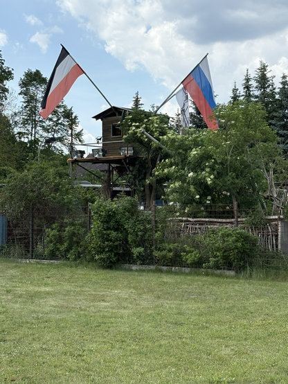 Baumhaus mit drei Flaggen, Russland, schwarz weiß rot und eine mit einem NS-Symbol