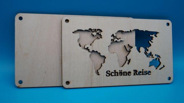 Zweiteilige Geldgeschenk-Verpackung aus Holz mit ausgeschnittener Weltkarte und Schriftzug „Schöne Reise“, geöffnet dargestellt.