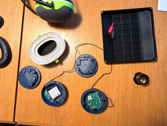 Rozmontowane słuchawki bluetooth JBL tak, ze zostały same głośniki z elektroniką połączone kabelkiem. W jednym (lewym) jest akumulator i mała płytka z elektroniką, w drugim (prawym) więcej elektroniki. Obok leży nausznik od słuchawek wygłuszających 3M.