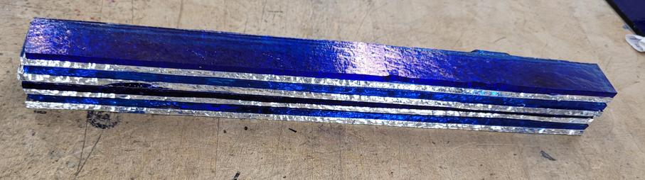 A 1 inch by 10 inch stack of 8 pieces glass that will be tack fused (fired to stick together but hold shape) and then cut up and used in other projects.  The colors are iridescent blue, turquoise blue, and deep royal blue, separated by clear sheets.