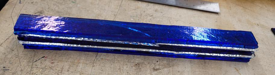 A 1 inch by 10 inch stack of 8 pieces glass that will be tack fused (fired to stick together but hold shape) and then cut up and used in other projects.  The colors are iridescent blue, turquoise blue, and deep royal blue, separated by clear sheets.