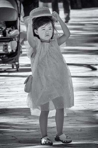 Little girl walks along Waikiki Beach in Hawaii, reaching to stop her hat from blowing off.