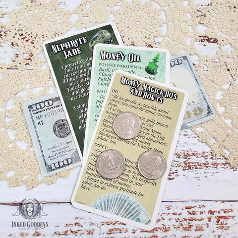 A set of 3 cards are arranged on a dark wooden tabletop. Each card in the "Money Spell Eclectic Witch Card Expansion Pack" features information on some of the Money Spell magick you can try, including info on Money Magick Dos and Don'ts, how to blend and use Money Oil, and info on Nephrite Jade. This is an exclusive product from Inked Goddess Creations.