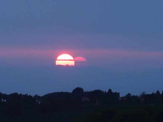 Rød sol på vej ned. Bag solen ses en lidt mørkere spejling af solen. Det ser ud som om der er to sole.