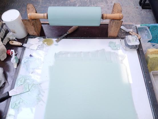 Encrier vert pistache pour pierre lithographique (carré d’encre lithographique étalée sur surface vitrée) et le rouleau recouvert de vert pour encrer la pierre . Outils divers autour.