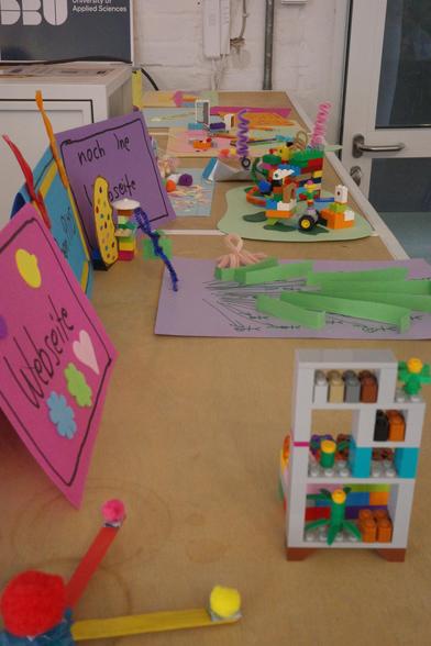 Foto: Auf einem Tisch steht viel buntes gefaltetetes und beklebtes Papier sowie kleinere Legobauten