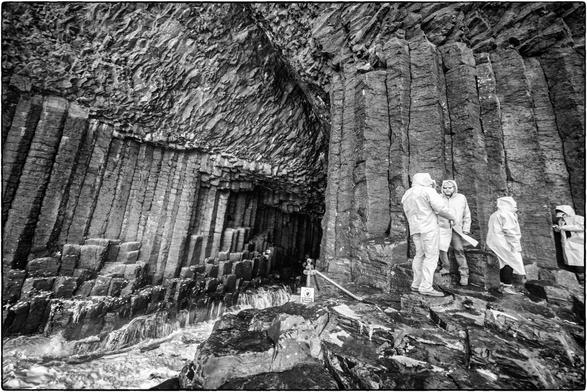 Schwarzweissfotografie des Eingangs zur Fingal's Cave auf der Hebrideninsel 
Staffa in Schottland mit vier Personen in Regenkleidern. 