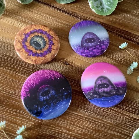 A photo of 4 badges showing little rocky spirits in sceneries that feature different pride flag colours.