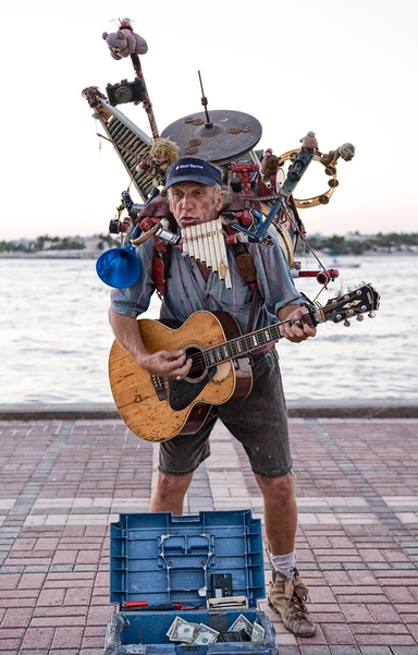 One man band playing guitar and other instruments.