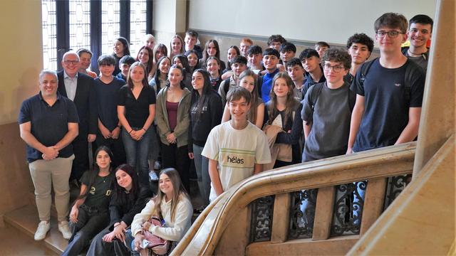 Oberbürgermeister Sven Schulze steht gemeinsam mit vielen Schüler:innen auf einer Treppe im Chemnitzer Rathaus. Alle lachen gemeinsam in die Kamera, um ein schönes Gruppenbild aufzunehmen. Im Hintergrund scheint ein helles Licht durch das Fenster.