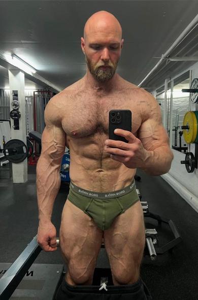 A muscular white guy taking a selfie at the gym with only his briefs on