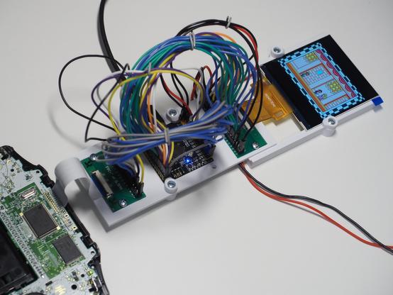 Gameboy Advance on the lower left connected to a RP2350B board behind a ratsnest of jumper wires which also connect a TFT on the right which shows some scene from a Mario game.