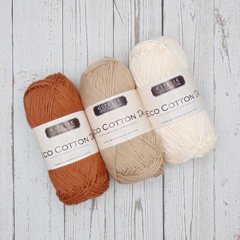 Close-up of 3 balls of cotton yarn in brown, beige and cream, laying flat on top of wood panels.