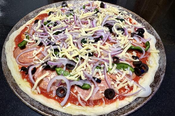 Assembled homemade pizza on a metal pizza pan ready to go in the oven.