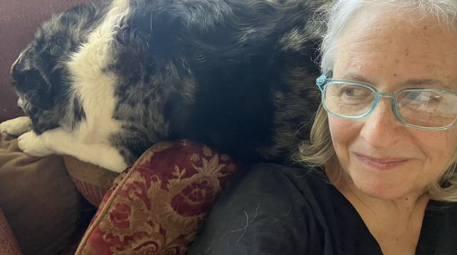 Photo of a smiling woman leaning against her black-and-white dog.