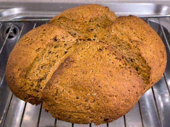 Auf einem Gitter liegt ein fertig gebackener Brotlaib. Es duftet nach frischem Brot.