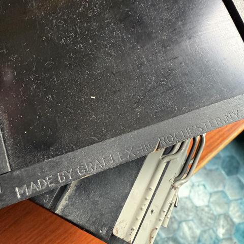 A close up detail of a vintage wooden film holder. The text embossed into the wooden edge of the holder reads:
Made by Graflex, Inc. Rochester, N.Y.