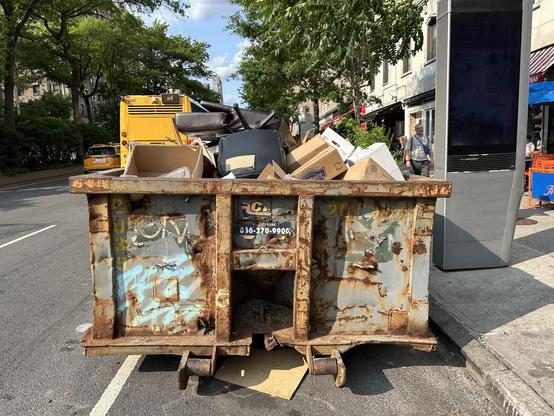 Picture of a curbside construction dumpster with boxes and furniture sticking up.
