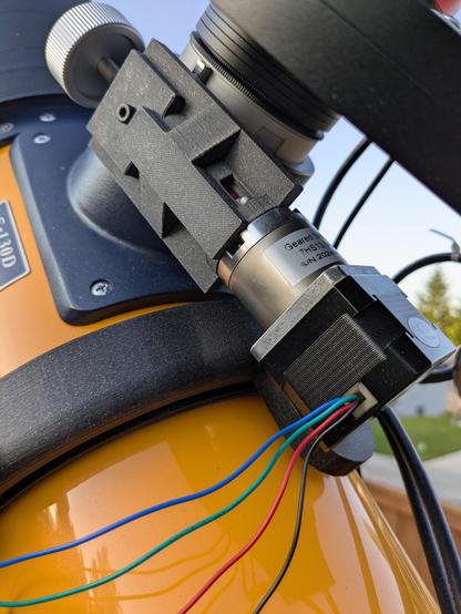 A stepper motor with a gearbox is mounted to a yellow-submarine colored telescope with a blocky black piece of plastic. The motor is attached to one side of the focuser knob, the normal manual focus knob can be seen in the top left of the image. Multicolor wires come from the motor and exit the frame to the bottom left.
