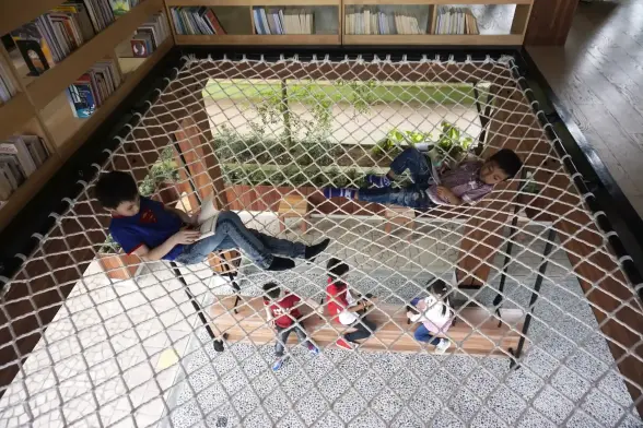 Two boys read laying on a netting ceiling.
