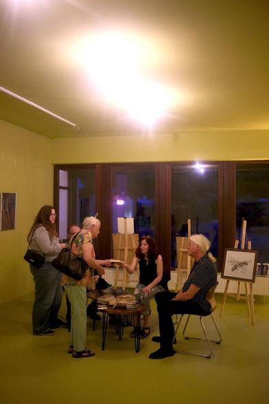 Fee überreicht einer Leserin ein signiertes Buch. Ringsum interessierte Leute.