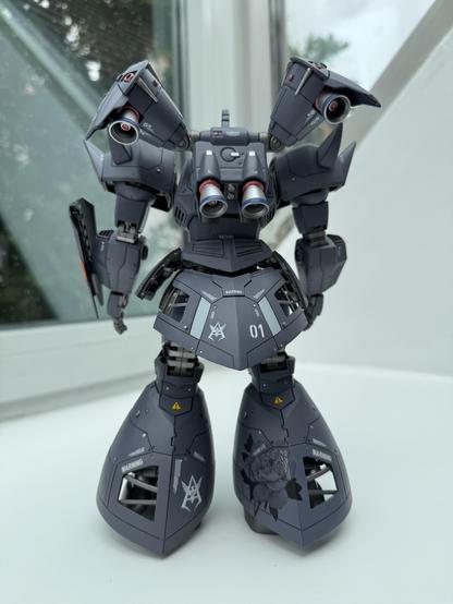 A detailed model of a robot, featuring a gray color scheme with red accents. The robot stands upright, showcasing notable features like twin exhausts on the shoulders and distinct markings, including warning symbols and a floral design on the legs.
