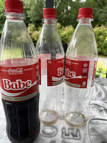 Drei Coca-Cola-Flaschen. Zwei leere, eine halb volle. Darauf die derzeitige Kampagne mit eher cringen Wörter. 

Auf allen drei Flaschen ist das Wort "Babe" aufgedruckt. Die zwei rechten Flaschen sind so gedreht, dass man liest:

"Babe, Baabe!" was an den alten Song von Take That erinnert