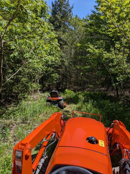 Pulling a lawn tractor out of the forest with a larger subcompact tractor
