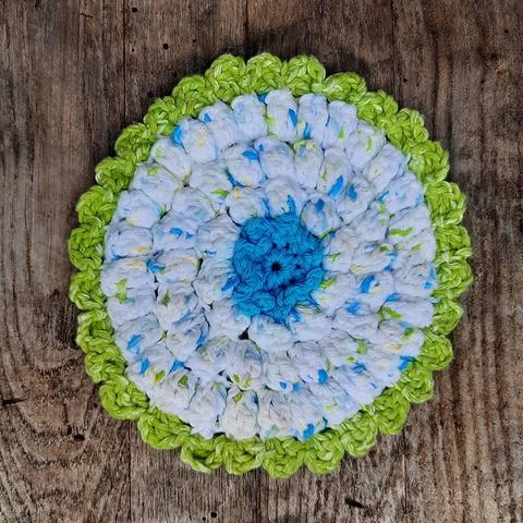 Top view of a crocheted hot pad sitting on top of a wood panel background.