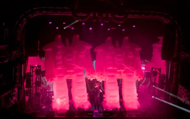 Photography of The Flaming Lips playing onstage. Wayne Coyne is singing in the middle of two giant inflatable pink robots.