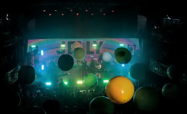 Photography of The Flaming Lips playing on stage. Multiple huge balloons are bouncing over the public.