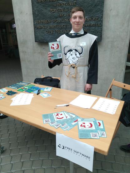 Me in church of emacs tabard and robe in front of desk with FSF & FSFE pamphlets and stickers