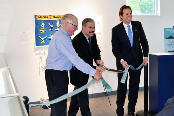 Three men standing, smiling, and cutting the ribbon to commemorate a new exhibit opening up at Albacore Park. The left and right men are holding the ribbon while the middle man is cutting it. 