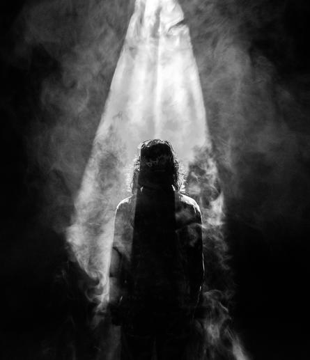 Jesus staring into dark clouds with a light shining upon him.
