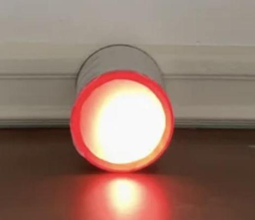 A glowing red circle on a table top. The glow is coming from a LED in a can with a cover in front of it. This is a device to show the current air quality by changing the color of a LED
