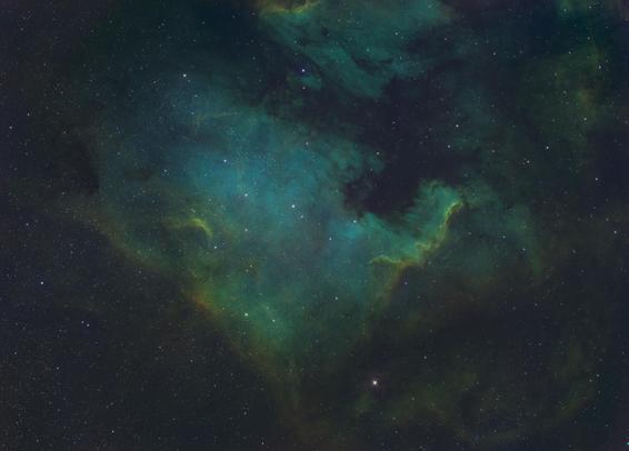 Image of the North America Nebula. The general cast of the image is teal-ish colored clouds in the background. An orange-yellow section of clouds extend from the middle left to the bottom middle of the image and also the area to the right of the center.