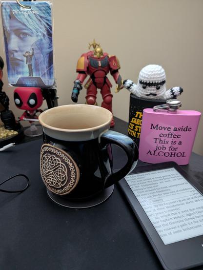 Picture showing a cup of coffee, various toys, a kindle and an alcohol flask 