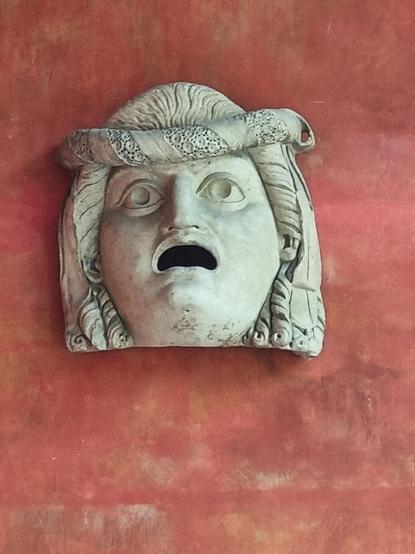 Head of a greek statue, face full of disgust, mounted to a red wall