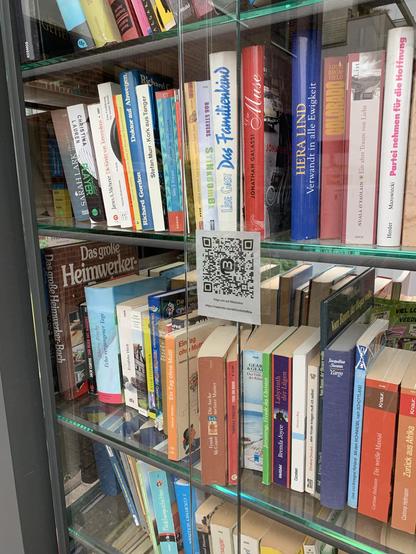 Auf dem Foto ist der neue qrcode zum Mastodon-Microblog als Sticker zu sehen, welcher auf die Glasschiebetür des Bücherschrankes angebracht wurde.