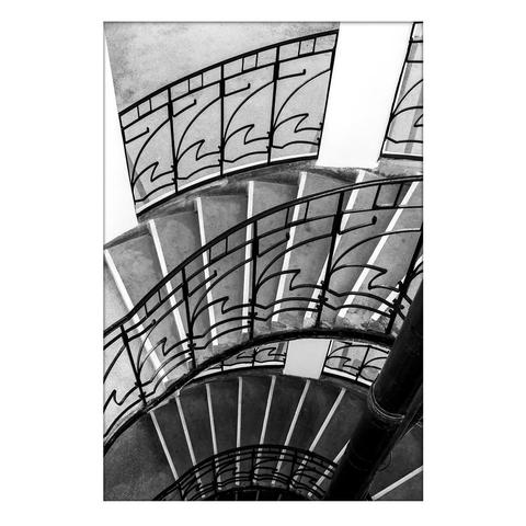 The spiral staircase inside an old water tower. A black and white image, the steps at the bottom are darker and the steps at the top become lighter. The steps are flanked by a decorative wrought iron railing. And the continuity of the staircase is sometimes interrupted by a whitewashed column.