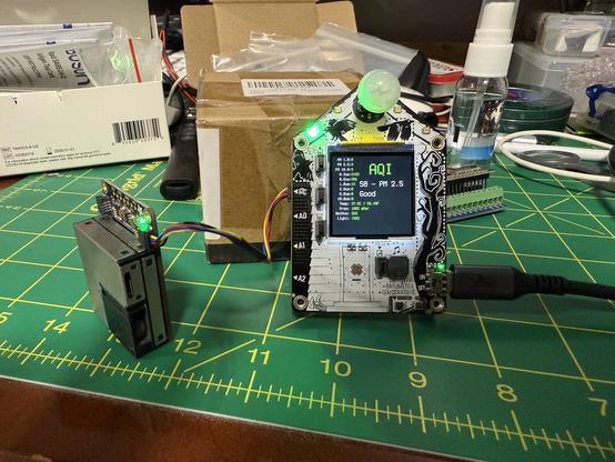 Particle sensor and funhouse dev board sitting on a cluttered surface.