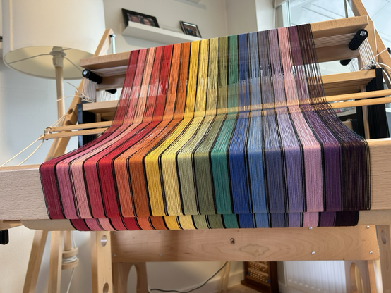 A close up look at the back of a handloom showing a rainbow striped warp fully wound onto the loom