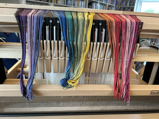 A look at the front of a handloom with the tail ends of a rainbow striped warp coming over the top, ready for threading